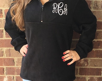 May include: Black fleece pullover with a quarter-zip neckline and white embroidered monogram. The long-sleeved top has a relaxed fit and is suitable for casual wear. The monogram features the letters R, C, and A in a cursive font.