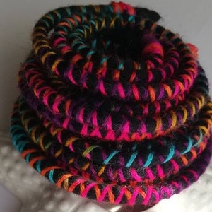 Könnte beinhalten: Ein farbenfrohes geflochtenes Band mit schwarzem, rosa, orangefarbenem und türkisfarbenem Garn, aufgerollt und auf einem weißen Keramik-Seestern präsentiert.