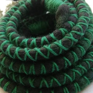 Puede incluir: Una serpiente de fieltro hecha a mano, enrollada, en tonos verdes y negros. El cuerpo de la serpiente es principalmente negro, con un patrón verde cosido que lo envuelve. La cabeza es negra y la serpiente está enrollada en forma circular.