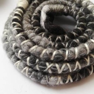 Può includere: Primo piano di un cordoncino intrecciato nero e grigio con cuciture bianche. Il cordoncino è avvolto a cerchio.