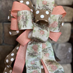May include: A brown, white and pink bow with a floral pattern and a rabbit design. The bow is made of three different ribbons, one with white polka dots, one with a floral pattern and one with a solid pink colour.