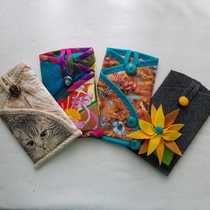 May include: Four different fabric phone cases with various patterns and colours. One case has a cat design, another has a floral design, another has a turquoise and purple design, and the last one is grey with a yellow flower.