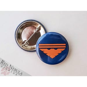 May include: A blue and orange button with a stylized bird design. The button is a 1 inch diameter pinback button.