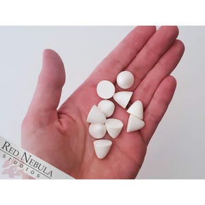 May include: A collection of white ceramic beads, including round and cone shapes, in a hand.
