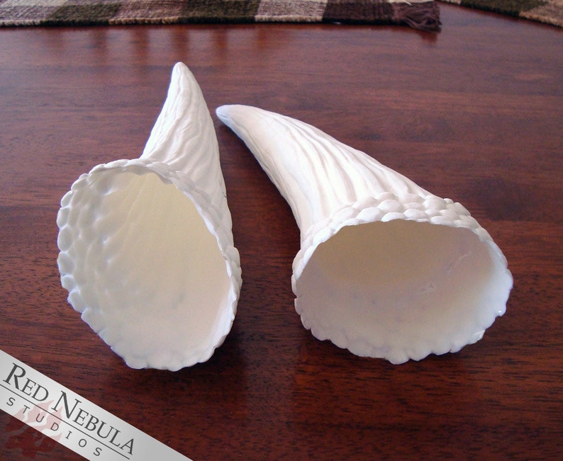 May include: Two white, ceramic horns with a textured surface. The horns are hollow and have a wide opening at the bottom.