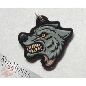 May include: A silver charm featuring a detailed illustration of a snarling wolf's head. The wolf has a gray and black fur pattern with a yellow eye. The charm is a great addition to a necklace or bracelet.