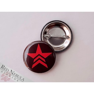 May include: A red star with three stripes on a black background. The star is a button with a metal pin on the back.