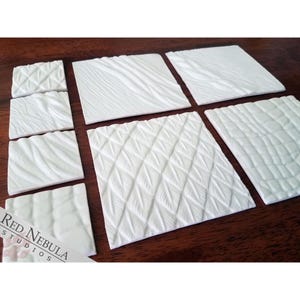 May include: Eight white textured tiles with different patterns. The tiles are arranged in two rows of four. The tiles are made of a smooth, white material and have a variety of raised patterns. The tiles are perfect for adding texture and detail to your miniature scenery.
