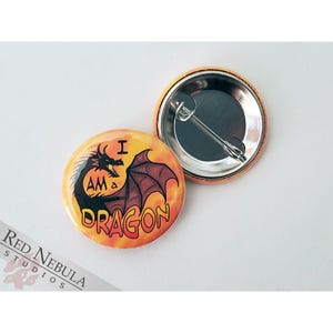 May include: A round button with a black dragon silhouette on a yellow and orange background. The text "I AM A DRAGON" is written in black letters.
