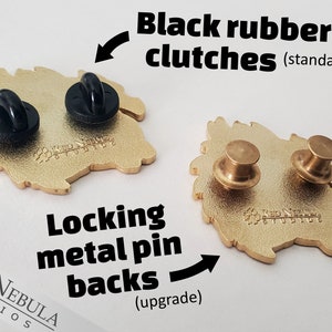 May include: Two gold-colored metal pins with different backings: black rubber clutches and locking metal pin backs. The pins have a detailed design and the text "Red Nebula Studios".