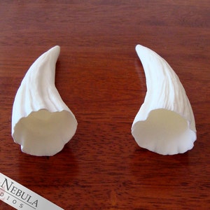 K&ouml;nnte beinhalten: Zwei wei&szlig;e, hohle, gebogene H&ouml;rner mit einer strukturierten Oberfl&auml;che. Die H&ouml;rner sind aus einem glatten, wei&szlig;en Material gefertigt und etwa 15 cm lang.