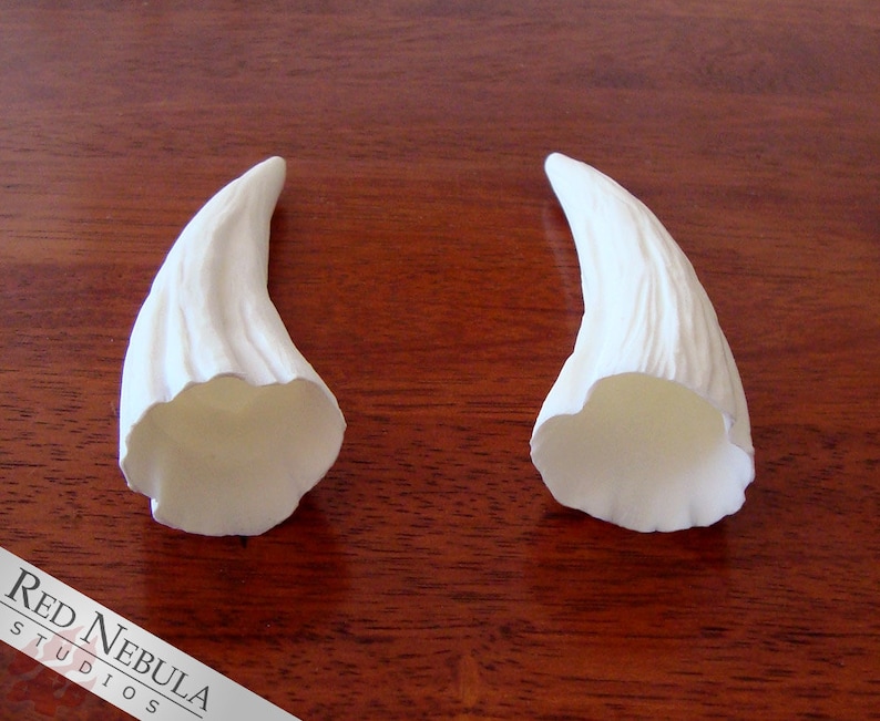 K&ouml;nnte beinhalten: Zwei wei&szlig;e, hohle, gebogene H&ouml;rner mit einer strukturierten Oberfl&auml;che. Die H&ouml;rner sind aus einem glatten, wei&szlig;en Material gefertigt und etwa 15 cm lang.