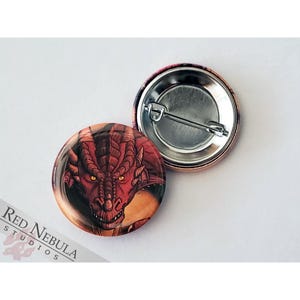 May include: Red dragon head button with a detailed illustration of a red dragon with yellow eyes. The button is round and has a silver pin back.