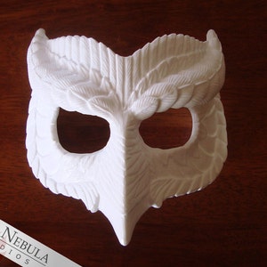 May include: White owl mask with detailed feather design. The mask has two eye holes and a beak.