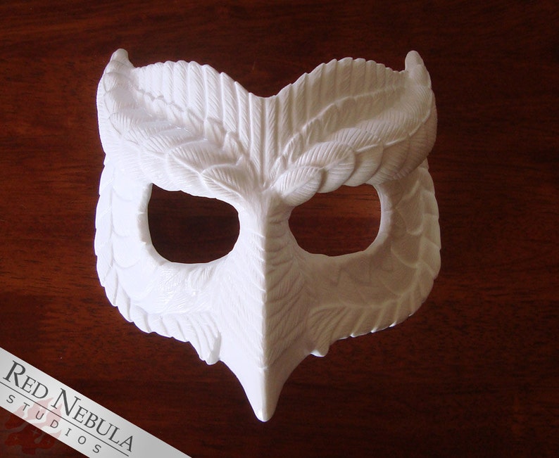 May include: White owl mask with detailed feather design. The mask has two eye holes and a beak.