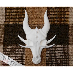 May include: White ceramic dragon skull wall decor with detailed features. The skull has a pointed snout, large horns, and a textured surface.