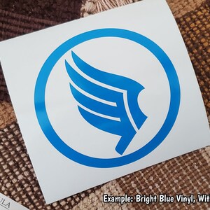K&ouml;nnte beinhalten: Ein hellblauer Vinyl-Aufkleber mit einem stilisierten Fl&uuml;gel, der von einem Kreis umgeben ist. Der Aufkleber befindet sich auf einem wei&szlig;en Hintergrund. Beispiel: Hellblauer Vinyl, mit Kreis