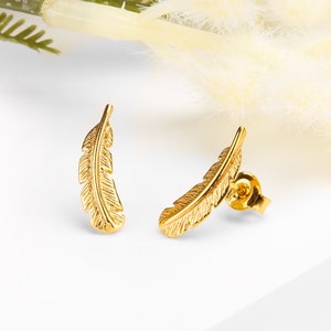 May include: A pair of gold feather stud earrings. The earrings are small and delicate, with a simple design.