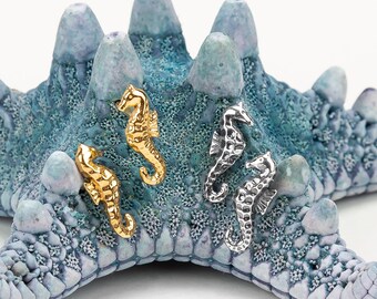 May include: Four seahorse charms, two gold and two silver, displayed on a blue starfish. The charms are small and detailed.