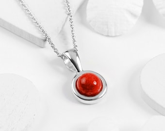 May include: A silver chain necklace with a red gemstone pendant. The pendant is round and has a silver bezel.