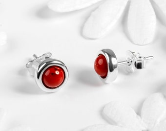 May include: A pair of silver stud earrings with red gemstone accents. The earrings have a simple, modern design.