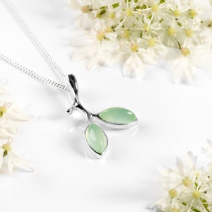 Può includere: Una collana d'argento con un delicato ciondolo a forma di ramo con due foglie di pietre preziose verde chiaro.