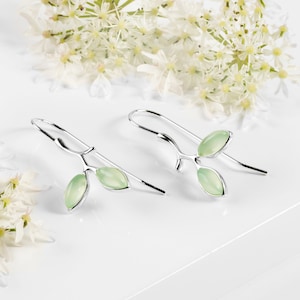 Puede incluir: Pendientes de plata con un delicado diseño de rama y tres hojas de piedras preciosas de color verde claro.