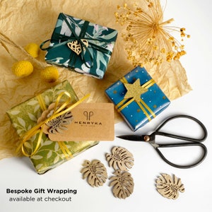 May include: Three gift boxes wrapped in different patterned paper. The boxes are on a brown paper background. The boxes are decorated with ribbons, a star, and a leaf. The text "HENRYKA with love" is on a brown tag attached to one of the boxes. The text "Bespoke Gift Wrapping available at checkout" is at the bottom of the image.