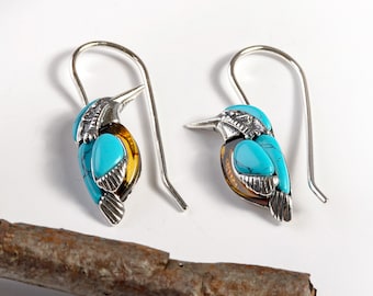 May include: A pair of silver dangle earrings featuring a turquoise and amber bird design. The earrings have a hook closure.