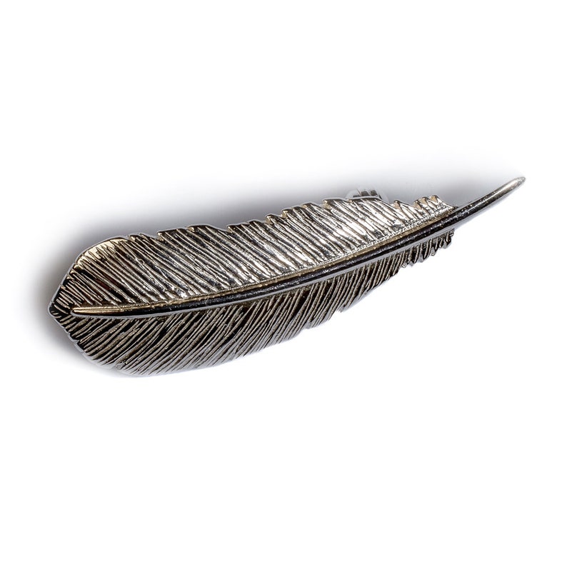 May include: A silver feather-shaped brooch with a detailed textured design.