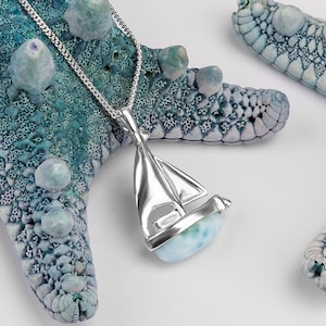 May include: A silver sailboat pendant necklace with a blue and green ocean jasper stone. The necklace is displayed on a blue and white starfish.