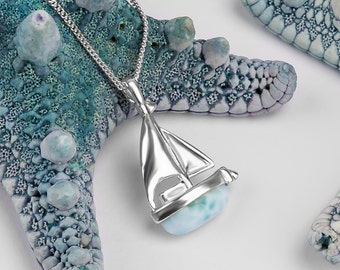 May include: A silver sailboat pendant necklace with a blue and green ocean jasper stone. The necklace is displayed on a blue and white starfish.