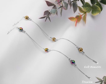 May include: Three silver chains with different colored beads. The top chain has gold beads, the middle chain has iridescent beads, and the bottom chain has iridescent beads. The chains are labeled "Gold Hematite" and "Titanium".