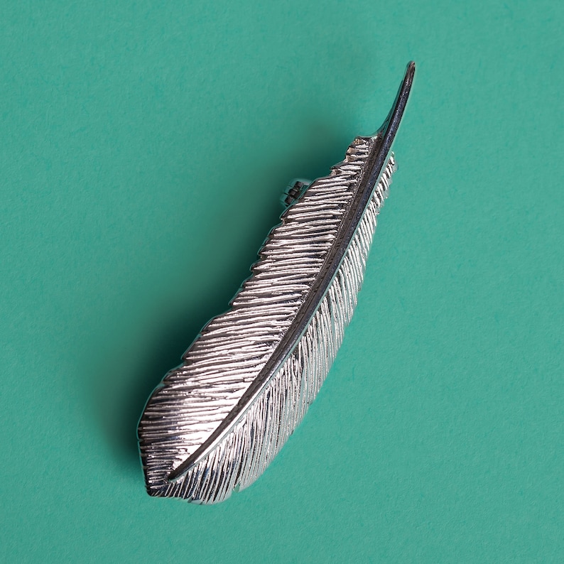 May include: A silver feather-shaped hair clip. The clip is detailed with a textured feather design.