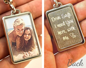 May include: A silver keychain with a photo on the front and an engraved message on the back. The photo shows a couple smiling at the camera. The message reads "Drive Safe I need you here, with me".