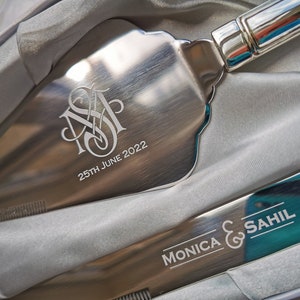 May include: A silver cake server with a monogram and the date "25th June 2022" engraved on the blade. The server is in a white box with a silver knife with the text "Monica & Sahil" engraved on the blade.