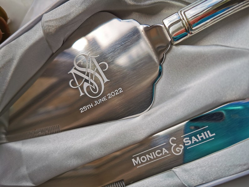 May include: A silver cake server with a monogram and the date "25th June 2022" engraved on the blade. The server is in a white box with a silver knife with the text "Monica & Sahil" engraved on the blade.