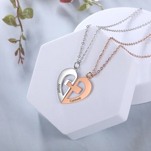 May include: Two heart-shaped necklaces, one silver and one rose gold, each with a cross design. The silver necklace is engraved with "Abigail," and the rose gold necklace says "Caldwell." Both necklaces are on delicate chains.