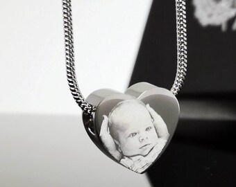 May include: A silver chain necklace with a heart-shaped pendant. The pendant has a photo of a baby engraved on it.