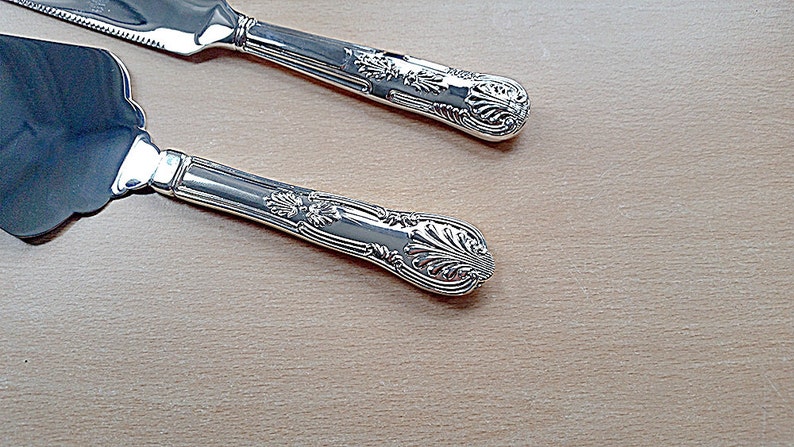 May include: Two silver cake servers with ornate handles. The servers have a decorative, floral design.