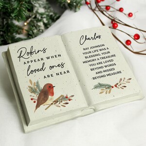 May include: A light-coloured, open book-shaped memorial plaque. The left page reads "Robins appear when loved ones are near" with a robin illustration. The right page reads "Charles" and a memorial message.