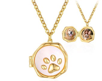 May include: A gold-colored necklace with a paw print pendant. The pendant opens to reveal two small photos. The necklace has a delicate chain and a round, gold-colored locket with a white background and a paw print design.