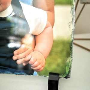 May include: A photo of two children, one holding the other, printed on a slate photo frame with a black stand.