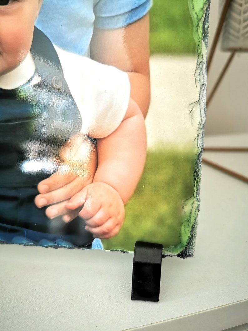 May include: A photo of two children, one holding the other, printed on a slate photo frame with a black stand.
