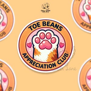 May include: Circular sticker with a cartoon paw print design. The sticker features a pink paw print with the words "TOE BEANS APPRECIATION CLUB" in a circular orange and pink design. Small pink hearts are also included.