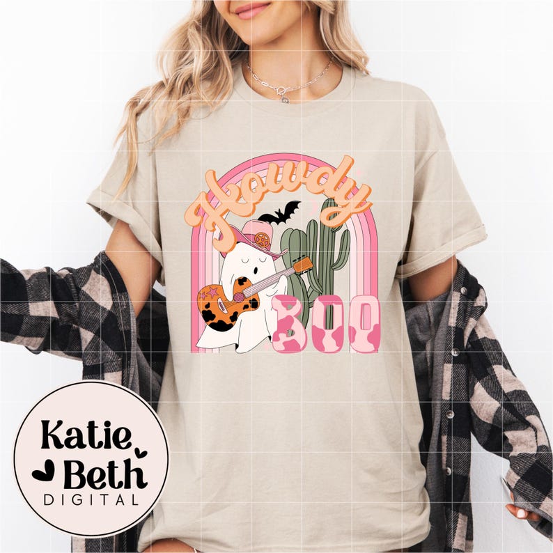May include: Beige t-shirt with a graphic featuring a ghost playing a guitar, wearing a cowboy hat, and the word "Howdy" above a rainbow. The word "Boo" is in pink with a cow print design. A cactus and bat are also included.
