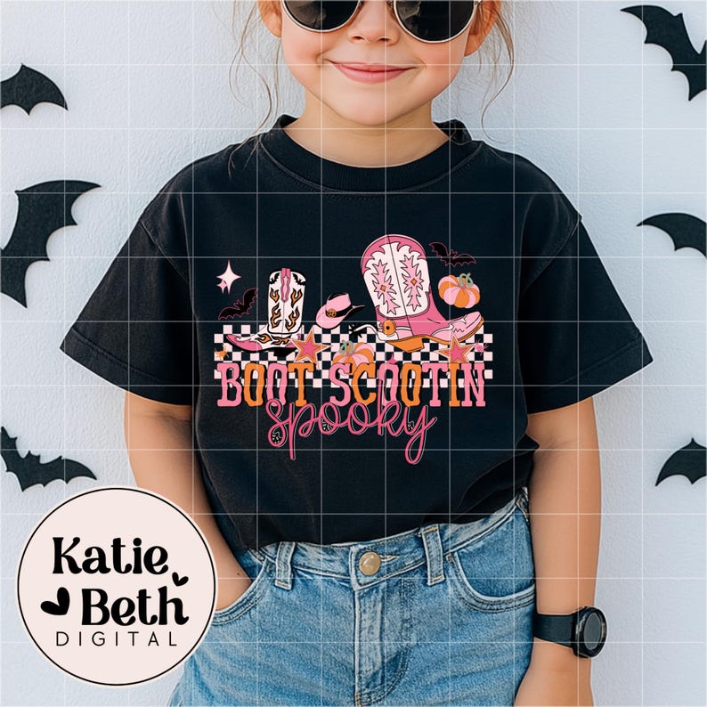May include: Black t-shirt with a colorful graphic design featuring cowboy boots, pumpkins, stars, and bats. The text "Boot Scootin' Spooky" is displayed in orange and pink. The shirt is worn by a child.