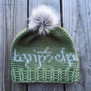 May include: Green crocheted beanie with a white pom pom and the word "bonjour" embroidered in white.