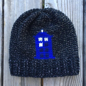 Puede incluir: Gorro de punto negro con purpurina plateada y un diseño TARDIS azul y blanco.