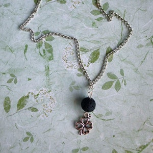 May include: A silver chain necklace with a black lava stone bead and a silver four-leaf clover charm.